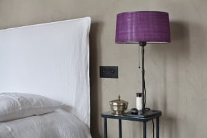 Mineralputz im Schlafzimmer in matt grün. weißes Bett und lila Lampe