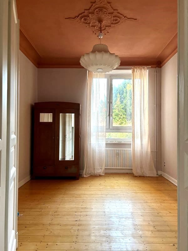 Altbauschlafzimmer mit rostroter Stuckdecke und hellen Wänden
